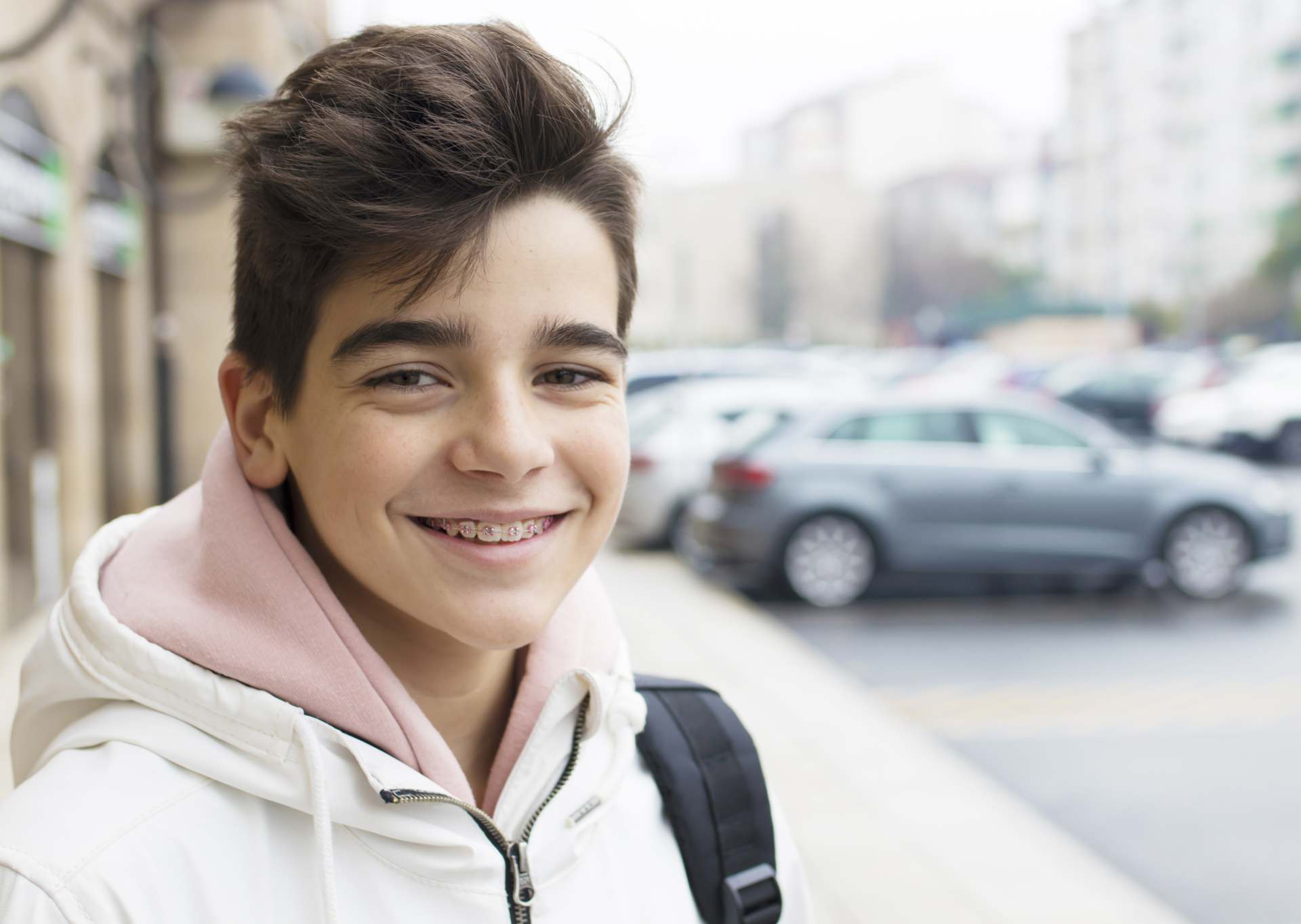Adolescent boy smiling with pink colored braces on a sidewalk on a cool fall morning